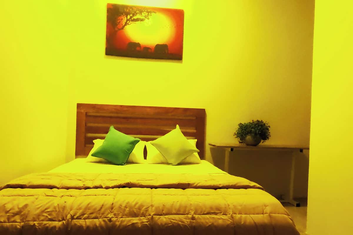A bed with a wooden headboard, two pillows, and a bedside table with a plant.