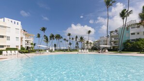 A swimming pool with clear blue water, surrounded by palm trees and white buildings with balconies.