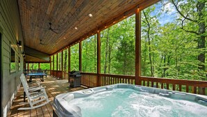 A wooden deck with a hot tub, rocking chairs, and a barbecue grill. - Family Fun Cabin Retreat w/ Arcade & Ping Pong (Broken Bow)