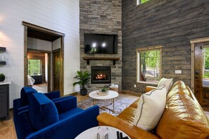 A cozy living room with a stone fireplace, blue and brown sofas, and a television mounted above it. - Family Fun Cabin Retreat w/ Arcade & Ping Pong (Broken Bow)