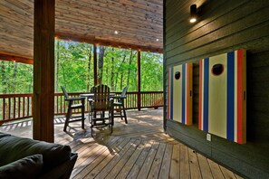 A wooden deck with a table and chairs, overlooking a forest. - Family Fun Cabin Retreat w/ Arcade & Ping Pong (Broken Bow)