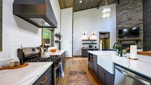 A modern kitchen with a central island, stainless steel appliances, and a rustic ceiling. - Family Fun Cabin Retreat w/ Arcade & Ping Pong (Broken Bow)