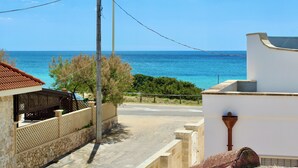 A coastal view with a clear sky, a road leading to the sea, and a building with a tiled roof.