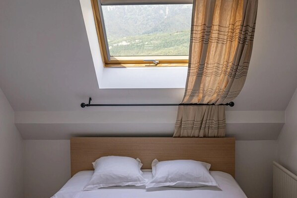 A bedroom with a wooden headboard, a window with a view of greenery, and a curtain.
