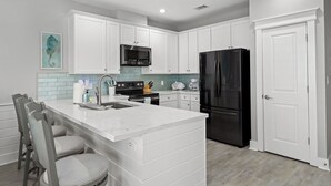 A modern kitchen with white cabinetry, a black refrigerator, a stainless steel microwave, and a marble island with bar stools.