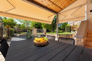 An outdoor patio with a table set for dining, surrounded by chairs, and a basket of fruit on the table. - Holiday Home Istarska (Rovinj)