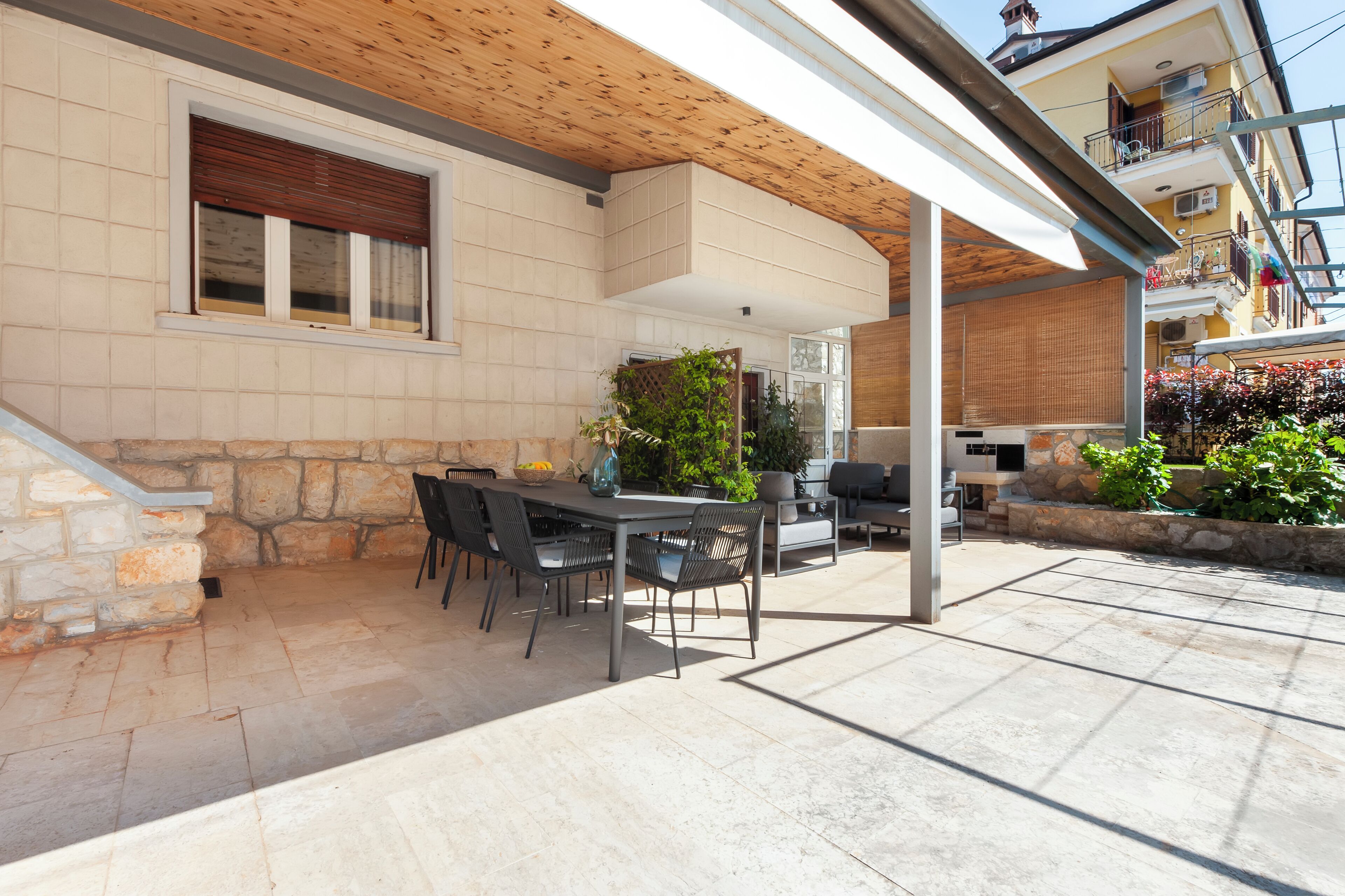 An outdoor patio with a stone wall, a wooden ceiling, and a table with chairs.