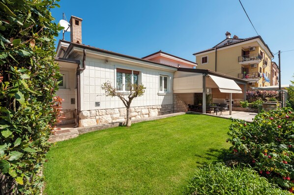 A residential building with a stone facade, a small lawn, and a balcony with outdoor furniture.