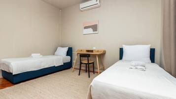 A hotel room with two single beds, a desk, a chair, an air conditioner, and a painting on the wall.