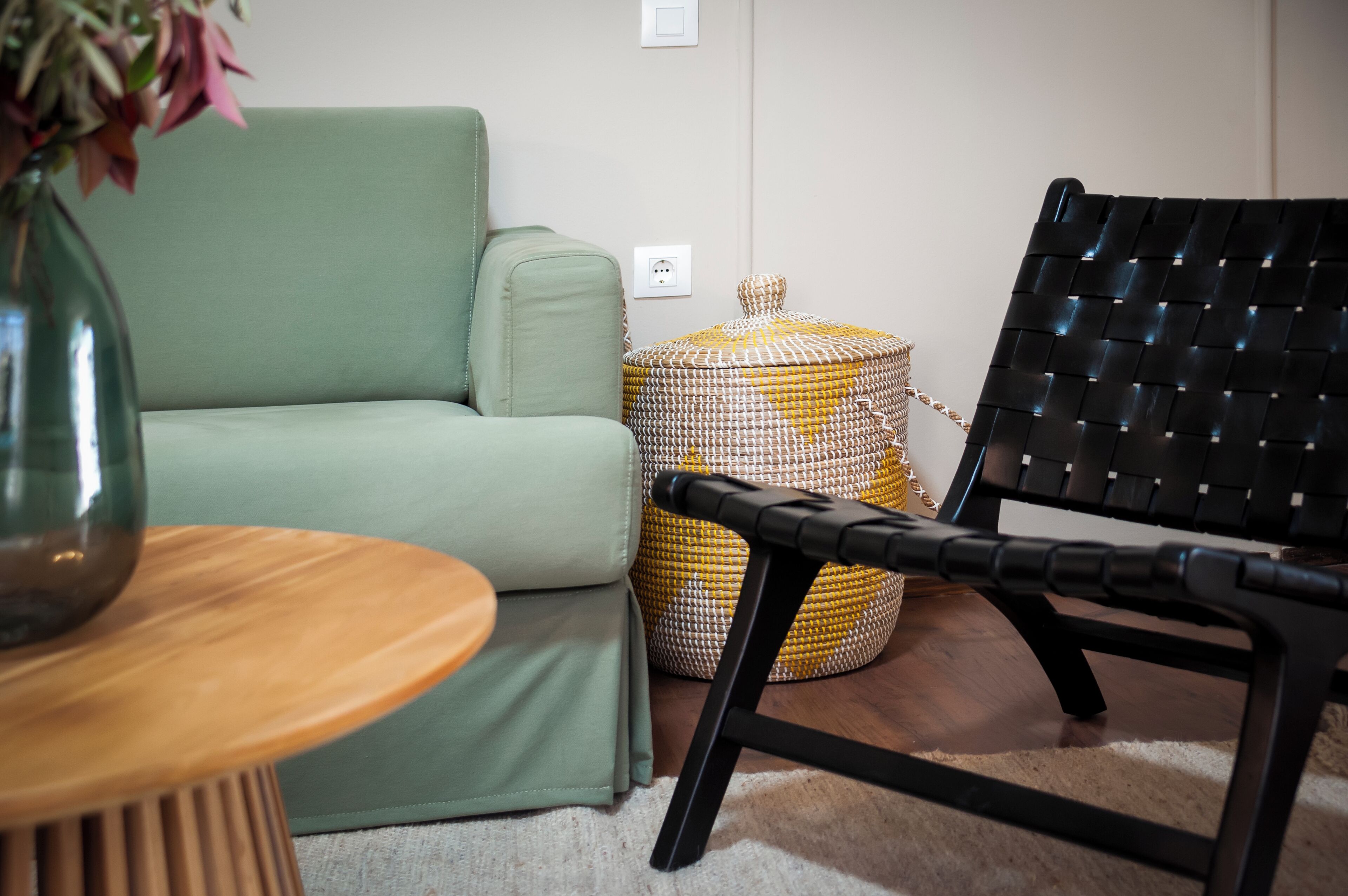 A green sofa, a black woven chair, a wooden side table, and a woven ottoman.
