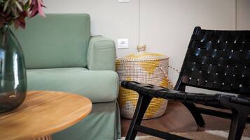 A green sofa, a black woven chair, a wooden side table, and a woven ottoman.