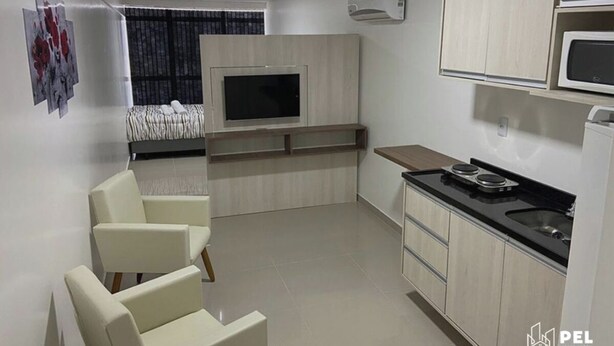 A compact hotel room with a kitchenette, a bed, a TV, and a seating area. - Pel Apart Hotel  (Pelotas)
