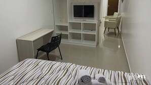 A hotel room with a bed, a desk, a TV mounted on a white cabinet, a chair, and a small seating area with chairs. - Pel Apart Hotel  (Pelotas)