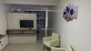 A modern living room with a flat-screen TV, a sofa, and a wall-mounted artwork. - Pel Apart Hotel  (Pelotas)