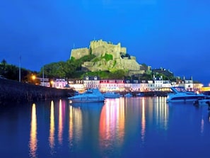 Un castillo histórico en una colina con vistas a un puerto y barcos amarrados.