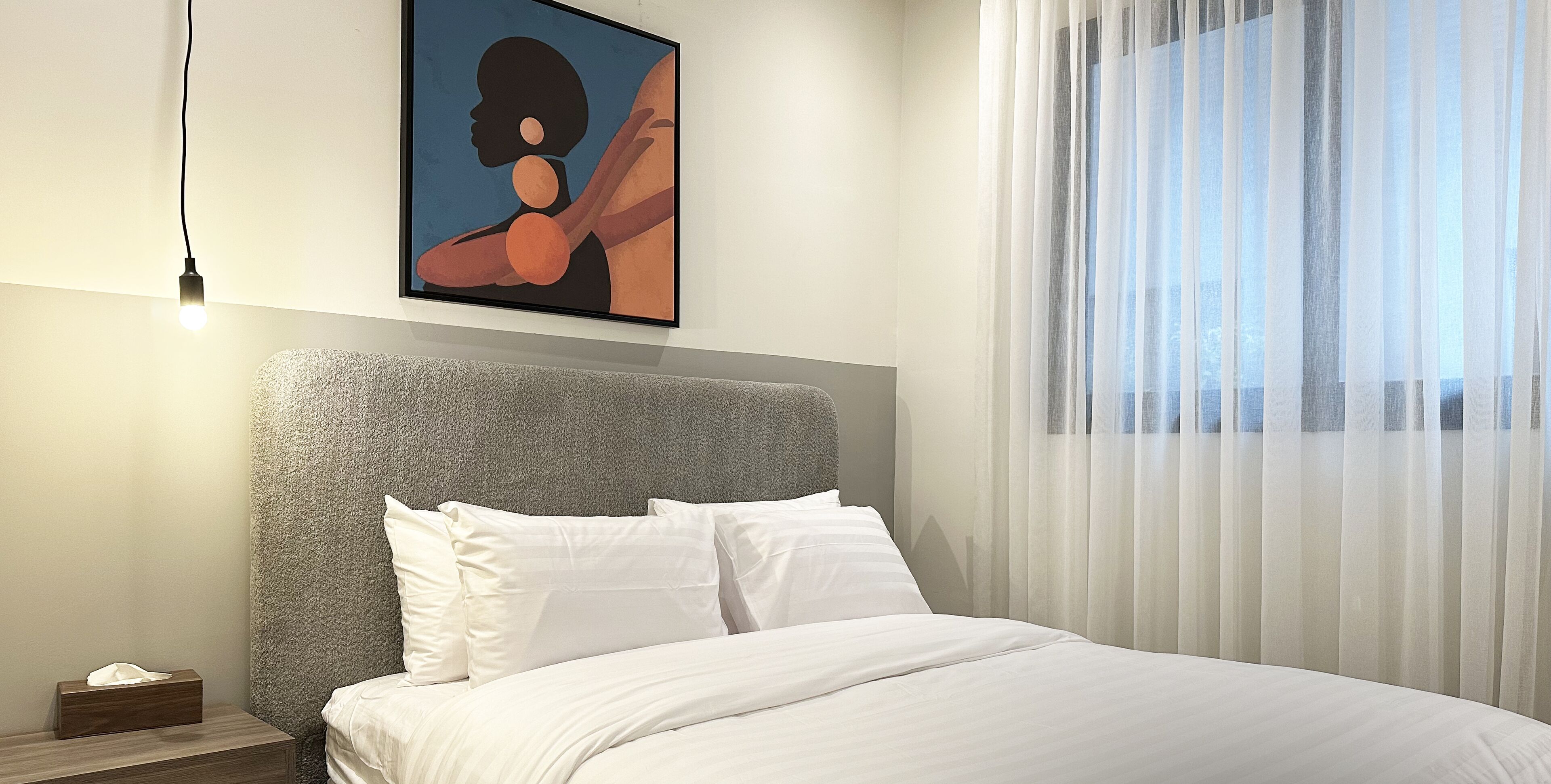 A modern bedroom with a large bed, a headboard, a bedside table with a tissue box, and a framed artwork on the wall.