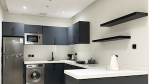 A modern kitchen with dark cabinets, a stainless steel refrigerator, a microwave, a washing machine, and a sink. - Kease Malqa D-1 Royal Touch  AX37 (Riyadh)