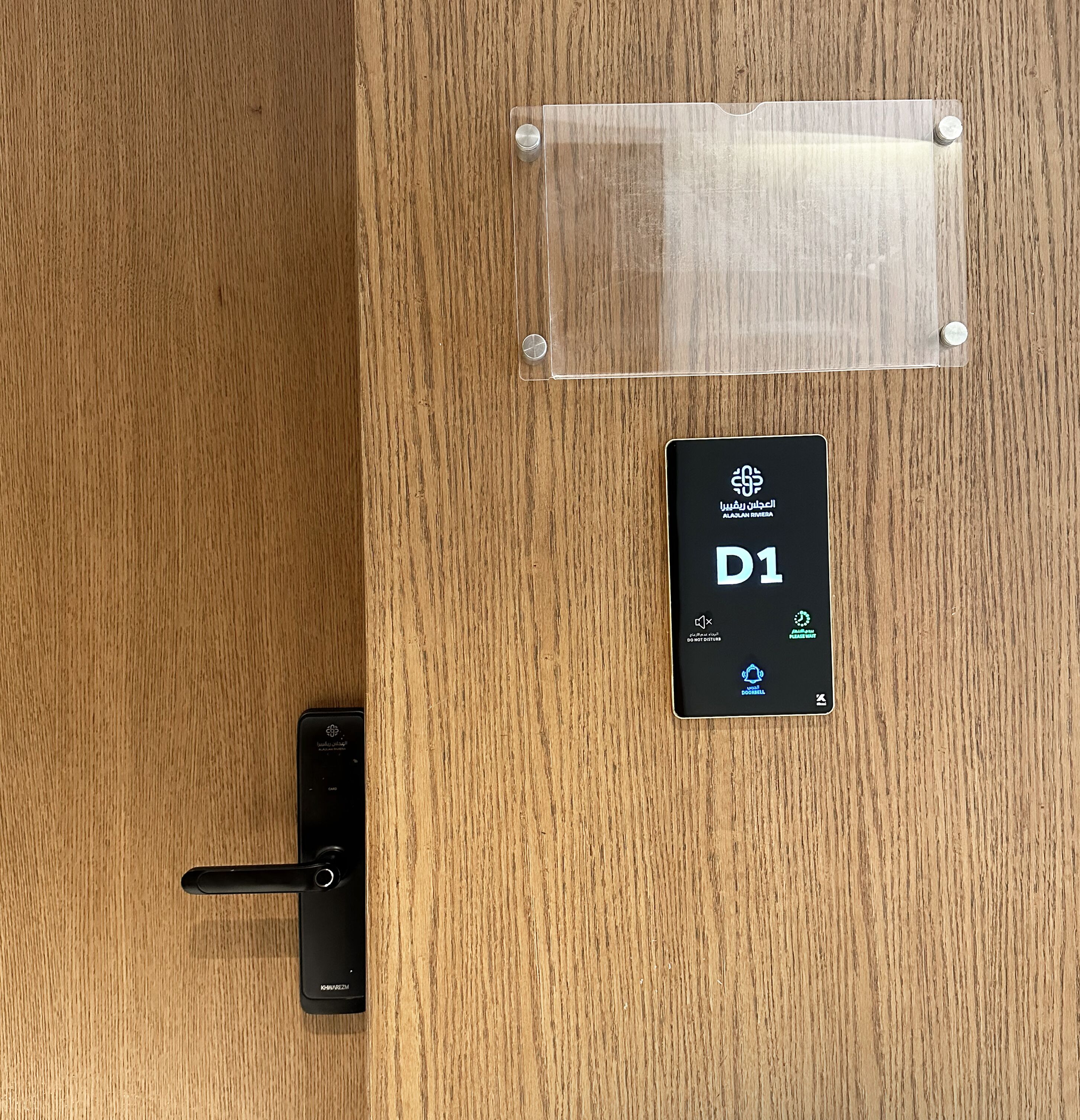 Une porte en bois équipée d’une serrure numérique et d’un lecteur de carte portant les inscriptions « ALQAN RIVERA » et « D1 ».