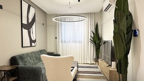 A modern living room with a grey sofa, a white armchair, a large plant, a TV, and a ceiling light. - Kease Malqa D-1 Royal Touch  AX37 (Riyadh)