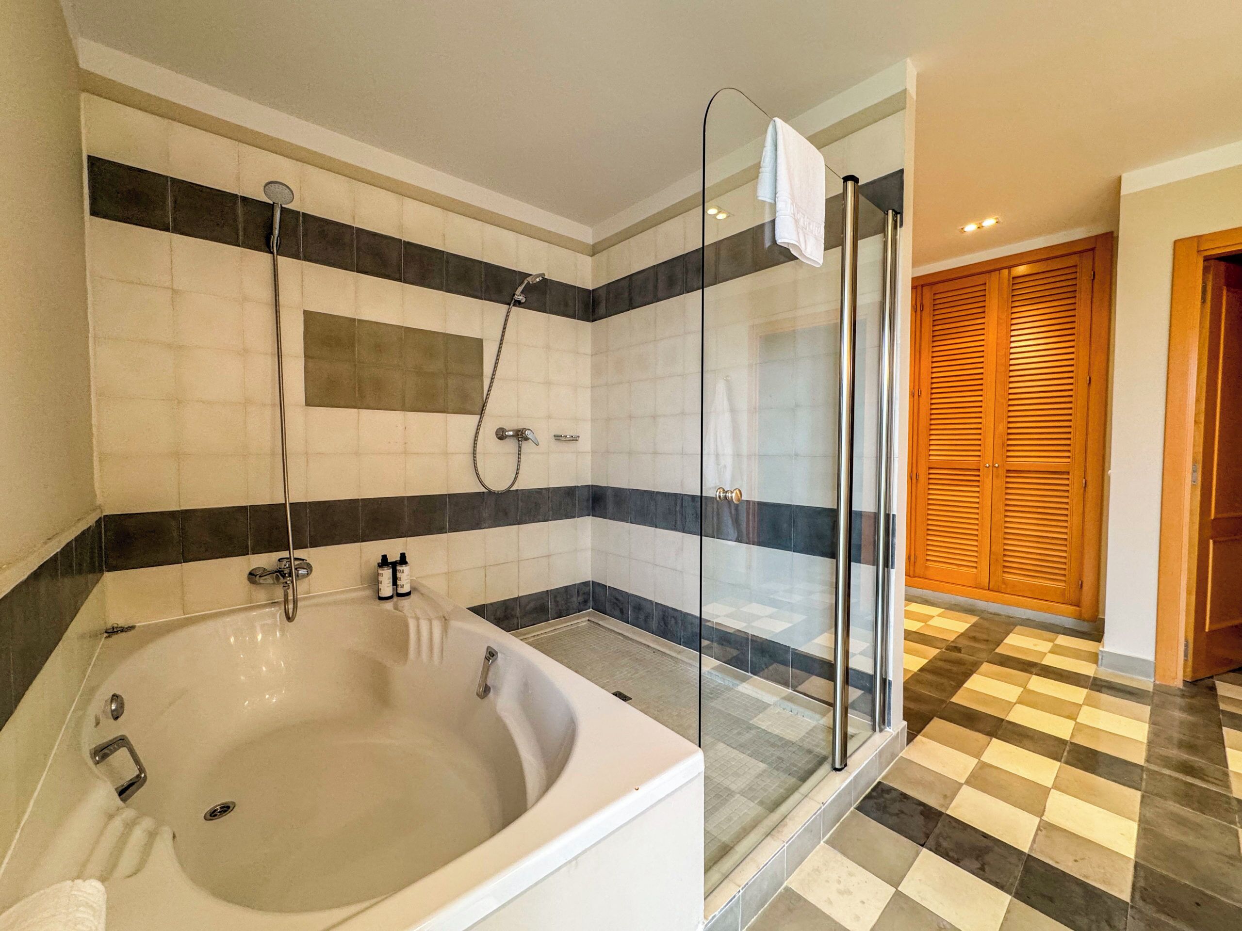 Un baño con una bañera grande, cabina de ducha con paredes de vidrio y piso a cuadros.