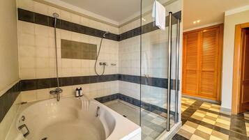 Un baño con una bañera grande, cabina de ducha con paredes de vidrio y piso a cuadros.