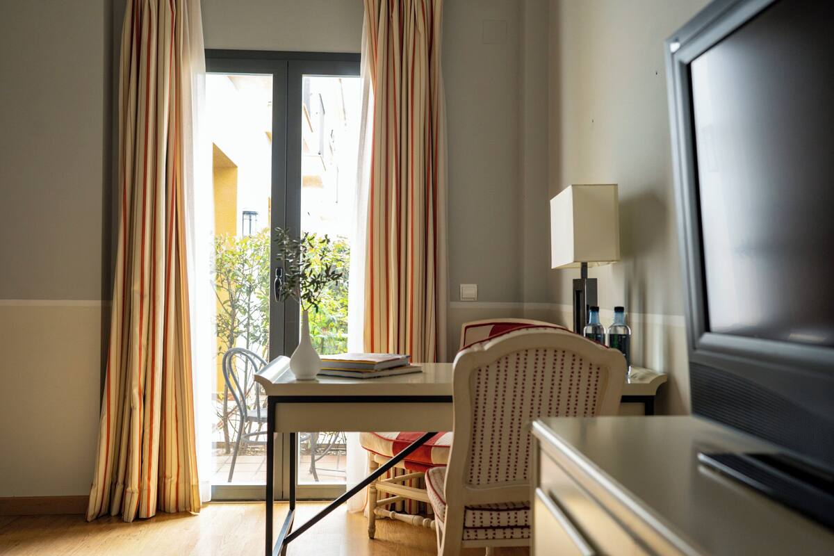 A hotel room with a dining table, chairs, a TV, and a lamp.