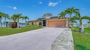 A residential house with a garage, a paved driveway, and palm trees.