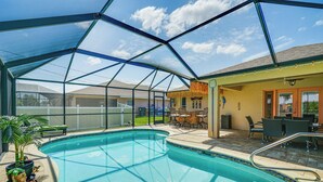 A swimming pool with a glass enclosure, outdoor seating, and a covered patio area.