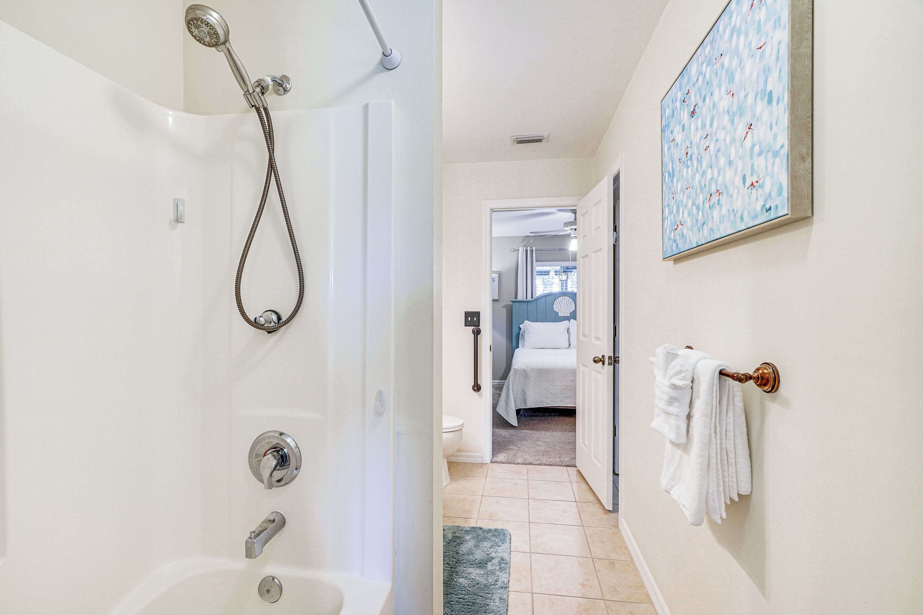 Ein Badezimmer mit Badewanne, Dusche und Toilette. Ein Handtuchhalter mit Handtüchern sowie ein Bild an der Wand sind vorhanden.