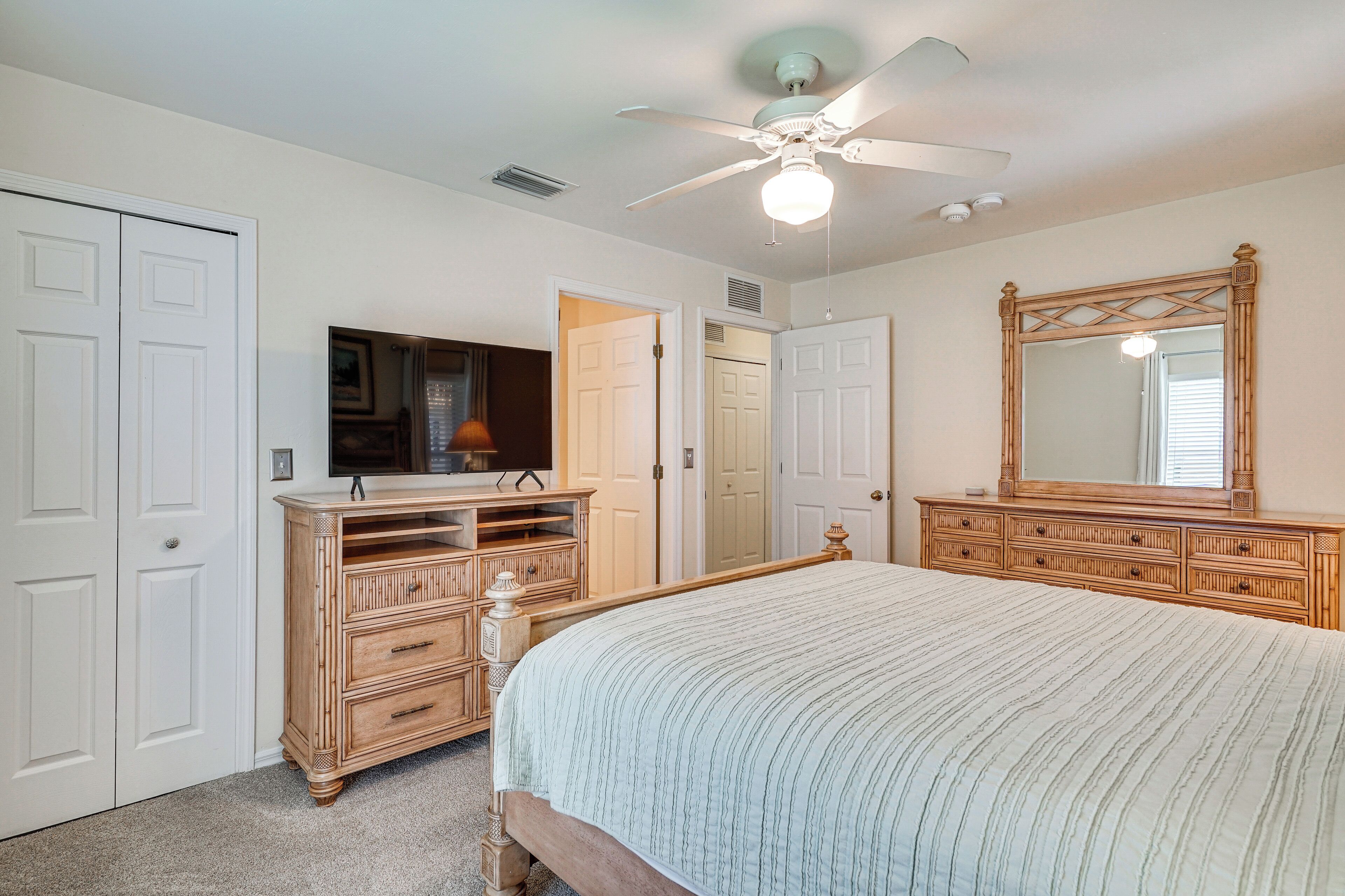 A bedroom with a bed, dresser, mirror, and ceiling fan.