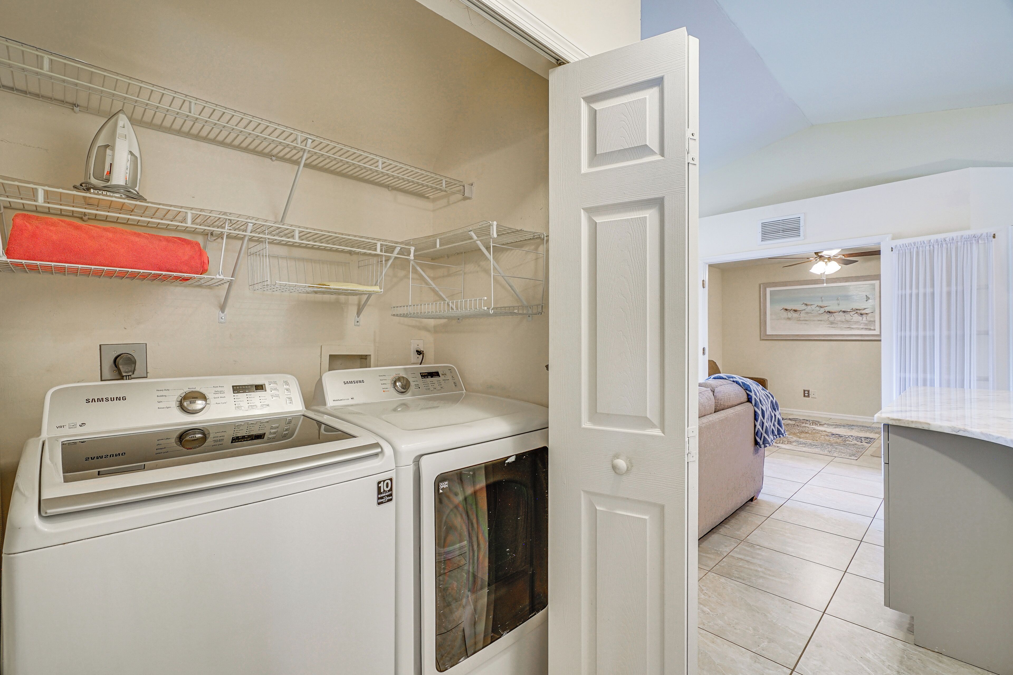Un cuarto de lavandería con dos lavadoras blancas, un tendedero y una puerta que da a una sala de estar con un sofá y un cuadro.