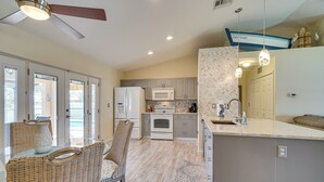 A modern kitchen with a dining area, featuring a ceiling fan, recessed lighting, and a view of the ocean through large windows.