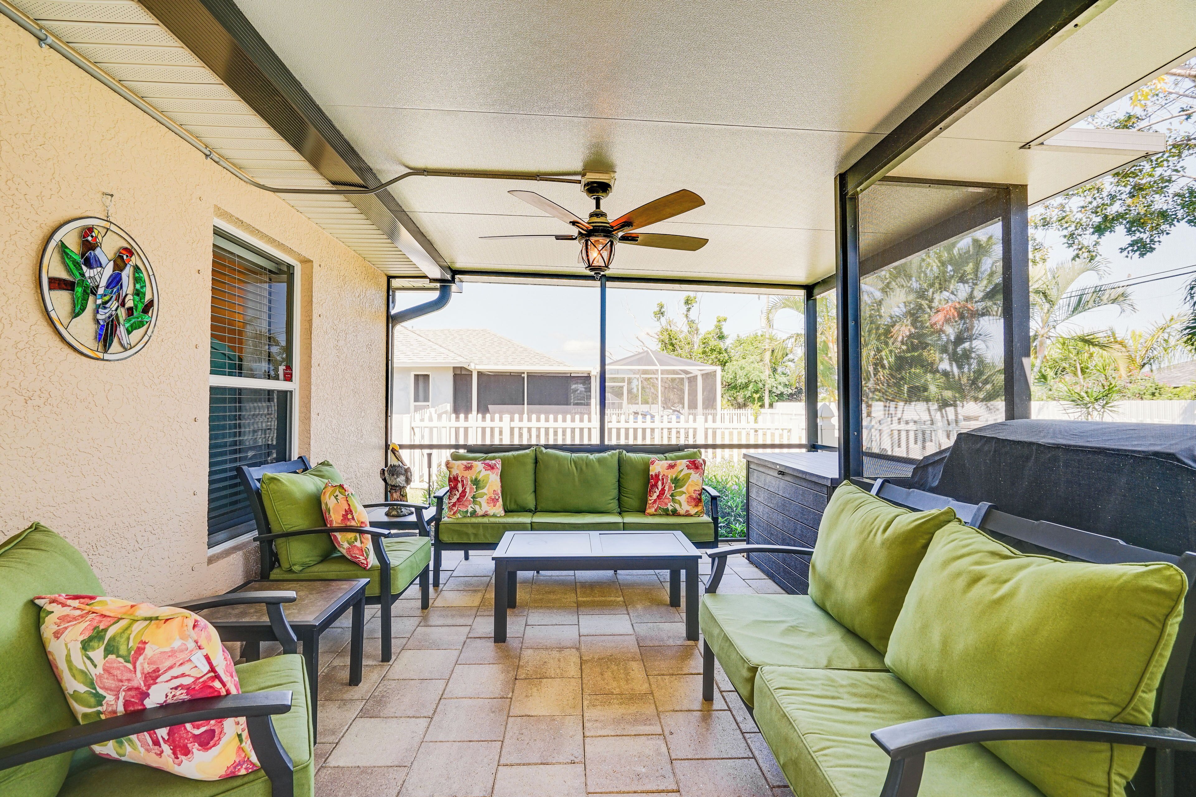 A covered patio area with green furniture, a ceiling fan, and a view of the backyard.