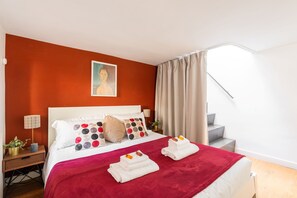 Habitación de hotel con una pared de acento roja, una cama con ropa blanca, un plaid rojo y un cuadro sobre la cama.