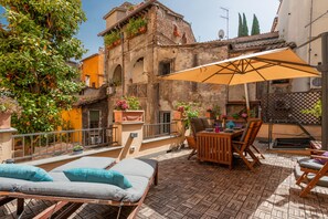 Une terrasse sur le toit, avec des chaises longues, une table en bois et des chaises, ainsi que des plantes en pot.