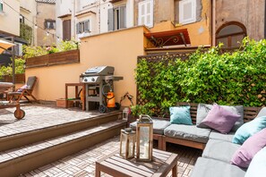 Un patio al aire libre con una parrilla, zona de estar y escalones que conducen a un balcón.