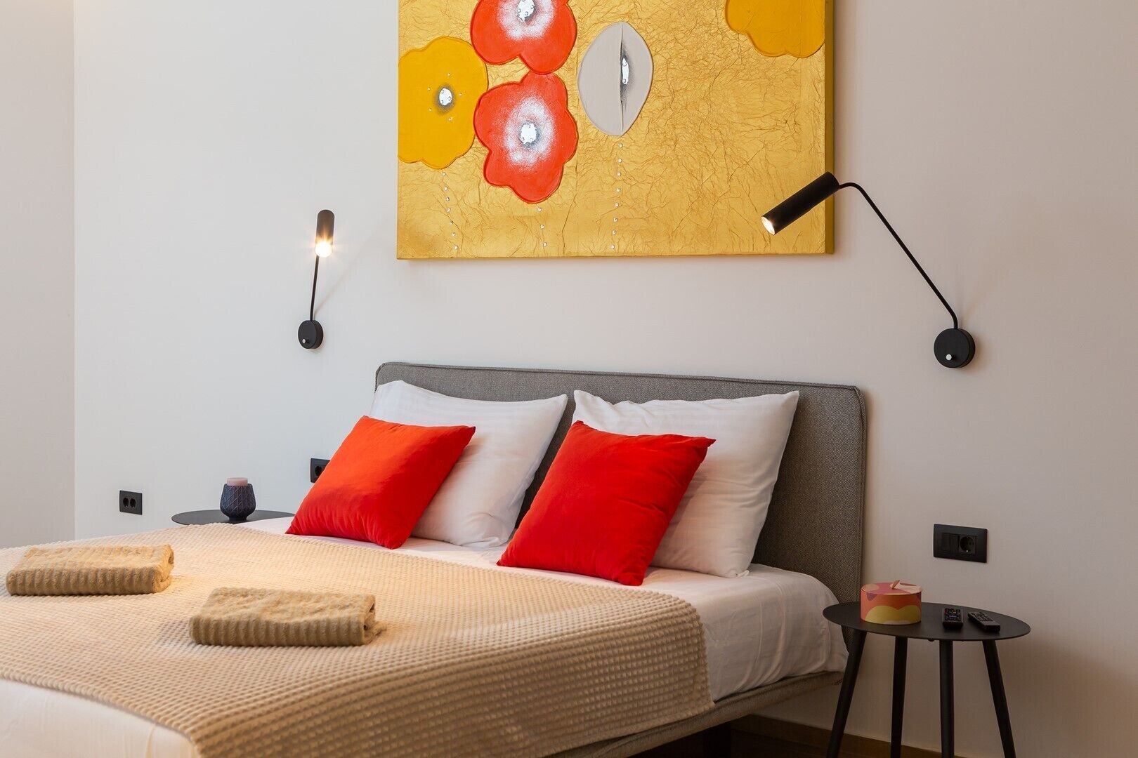 A modern bedroom with a bed, pillows, a bedside table, a lamp, and a wall art piece.