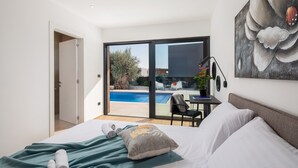 A modern hotel room with a large bed, a desk, and a view of a swimming pool. - Luxury villa with swimming pool and sauna near Pula. (Vodnjan)