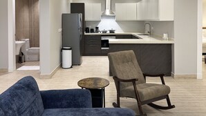 Eine moderne Küche mit einer zentralen Kochinsel, einem Essbereich mit einer Couch und einem kleinen Tisch sowie einem sichtbaren Mülleimer.
