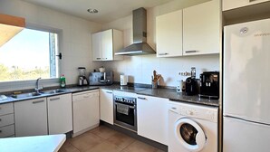 Une cuisine moderne avec des meubles blancs, un four encastré, un lave-linge et un réfrigérateur.