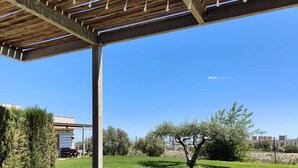 Une terrasse extérieure avec une table dressée pour deux personnes, une carafe d’eau et un saladier de fruits.