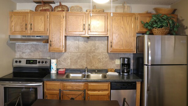 A kitchen with wooden cabinets, a stainless steel refrigerator, a stove, and a dishwasher.