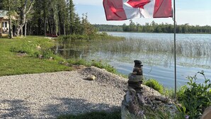 A flagpole with a Canadian flag, a lake, and a stone wall in a park setting. - Welcome to the Lake House (Wiarton)