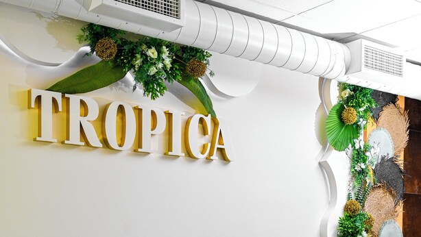 A restaurant interior with a wall-mounted sign reading "TROPICA," a buffet counter with a decorative plant arrangement, and a seating area with tables and chairs. - Tropica Inn Hotel (Yerevan)