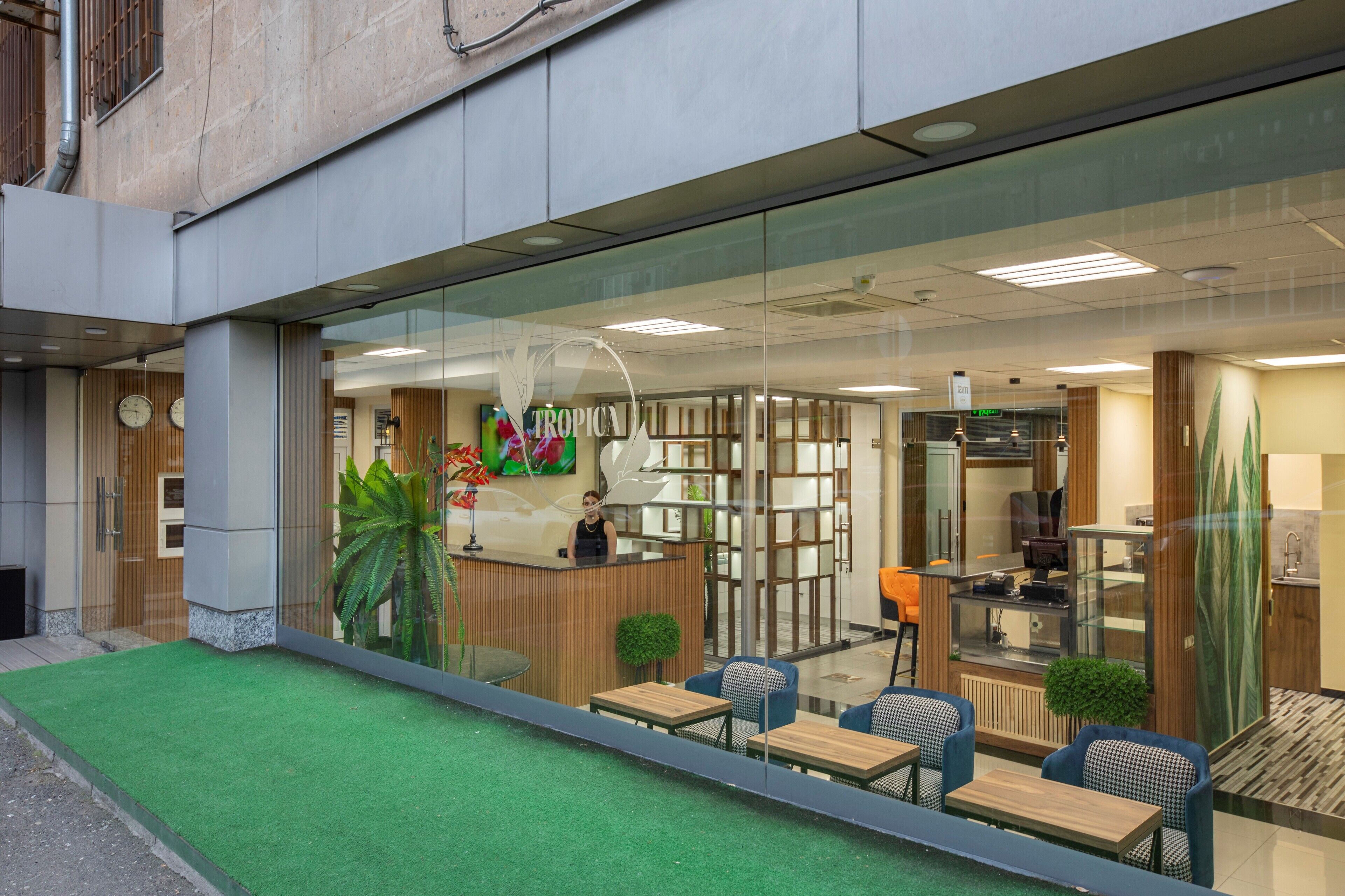 A modern indoor space with a reception desk, seating area, and a kitchen visible through glass partitions.