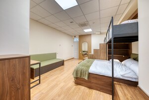 Een kamer met een stapelbed, een groene bank, een houten kast en een spiegel.