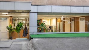 A modern hotel entrance with a glass facade, a green awning, and a visible reception area. - Tropica Inn Hotel (Yerevan)