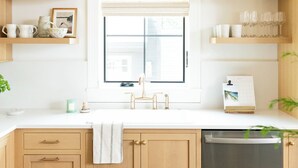 A kitchen with wooden cabinets, a window with blinds, a sink, and a dish drying rack.