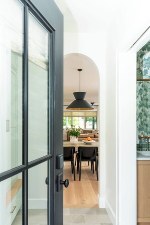 Una cocina moderna con comedor, que presenta una puerta de vidrio con marco negro, una lámpara colgante y vistas del comedor a través de la puerta.