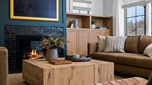 A cozy living room with a fireplace, a wooden coffee table, a brown sofa, and a bookshelf.